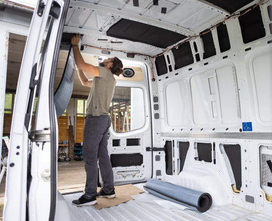 Mann klebt Dämmmaterial im Inneren eines Campervans an die Decke und Wände.